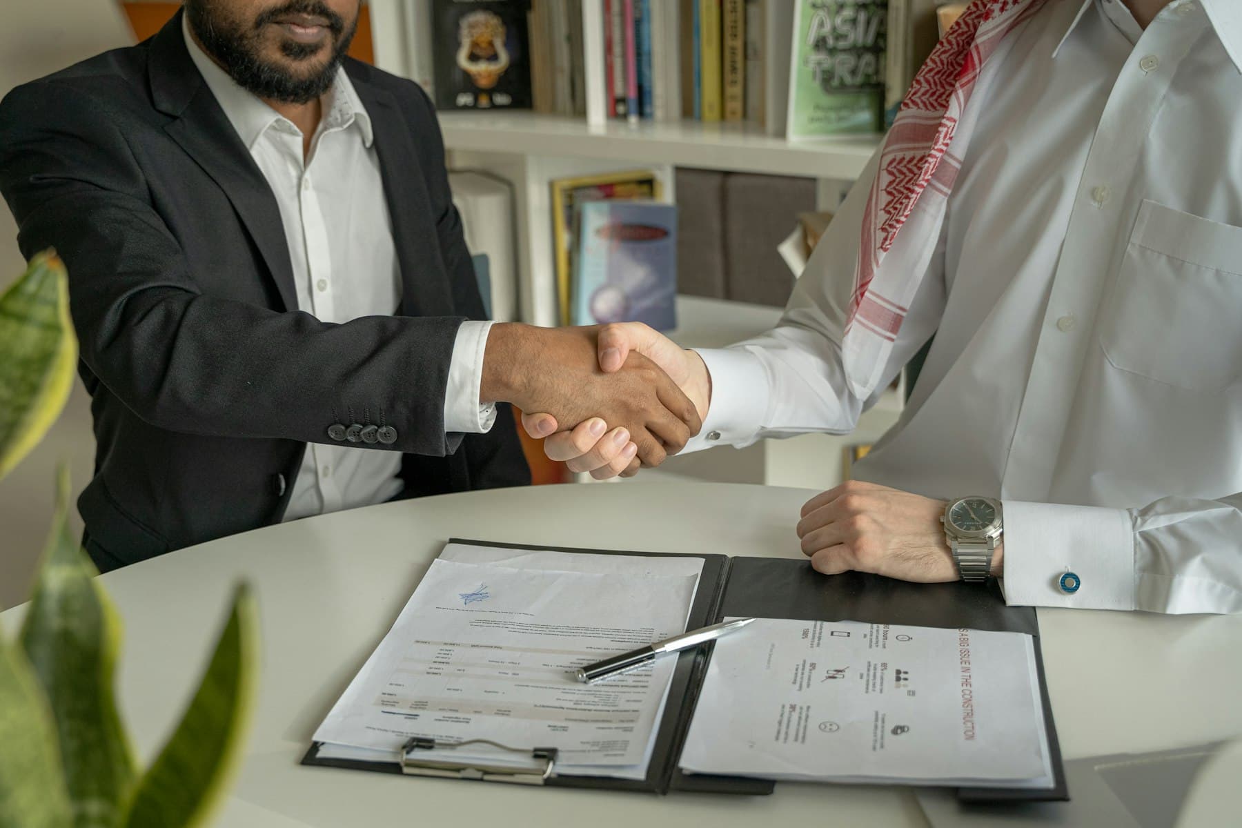 مصافحةٌ بين رجل أعمال ورجلٍ بالزي القطري فوق عقدٍ موقّع على الطاولة — شركةٌ جديدة تبدأ من أول اتفاق